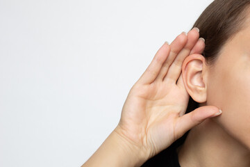 Fototapeta premium A woman puts her hand to her ear and listens, isolated on a white background with copy space. Hearing problems, ear diseases, noise. Concept of testing and hearing loss, audiometry