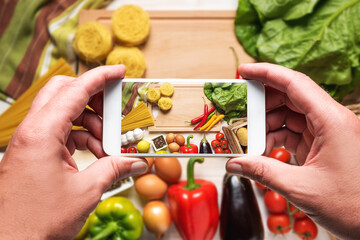 Woman hands taking a photo of colorful vegetables and noodles on wooden background. Food concept.