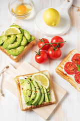 Variation of healthy breakfast toasts with avocado and cherry tomatoes on white wooden background. Food concept.
