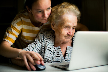 A young woman teaches her grandmother how to use a laptop, bridging the generational gap with patience and love.