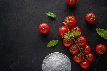Fresh cherry tomatoes on a black background with herbs. Food background. Top view.
