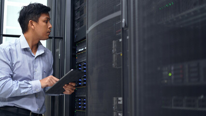 A technician in a blue shirt uses a tablet while inspecting a server rack in a modern data center, ensuring proper functionality.