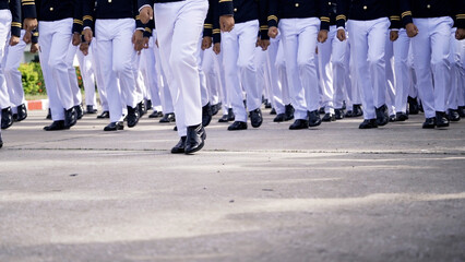 A group of cadets dressed in formal uniforms, marching in synchronized formation on a paved road during a military parade or drill.