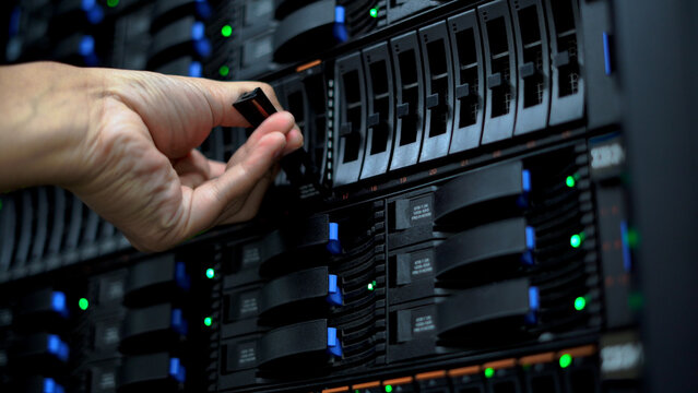 Close-up of a technician's hand replacing or adjusting a hard drive in a server rack at a data center.  