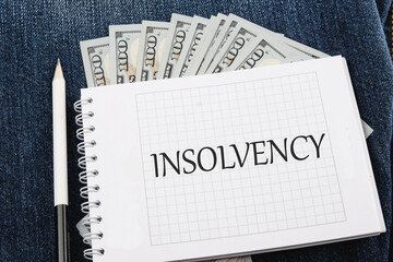 Debt relief concept. A word INSOLVENCY on a notebook lying on jeans with dollar bills