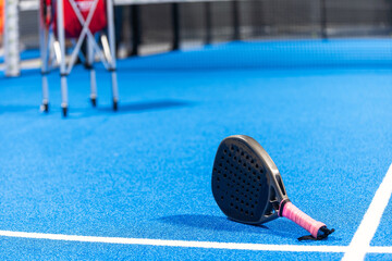 Black professional paddle tennis racket and ball with natural lighting on blue background....