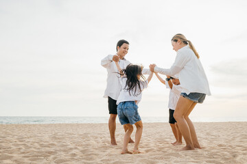 Pure happiness captured on beach as an Asian family father and mother holding children jump into air. beautiful ocean background adds touch of serenity to this lively portrayal of family fun.