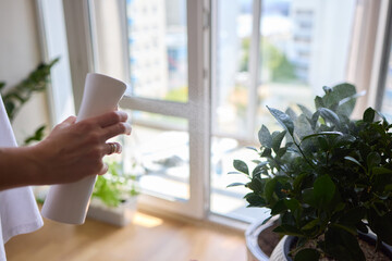 A person outdoors is using a spray bottle to water a plant in a garden