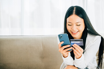 Smiling woman with smartphone and credit card shops online on sofa. Engaged in ordering banking and buying goods or services. Modern technology for convenient shopping at home.