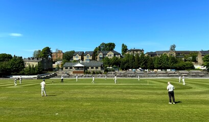 Players on a green cricket field, under a blue sky poised in readiness, in anticipation of the next play near, Bacup Road, Rawtenstall, UK