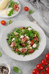 Fresh summer salad with arugula, melon, prosciutto and mozzarella cheese on concrete background, Healthy food. Top view.