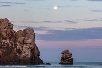 Morro Rock at dawn, Morro Bay, California. Full moon in the colored sky with streaks of clouds....