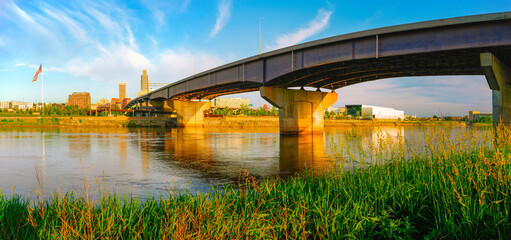 Omaha City Skyline, I-480 Missouri River Bridge, and gentle water flow at warm glowing sunrise: A...