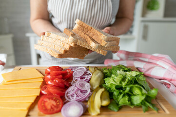 Woman preparing or making sandwiches for lunch with cheese and vegetables and whole wheat toast