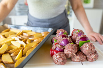 Woman preparing healthy meal with minced meat skewers and potato wedges in the kitchen