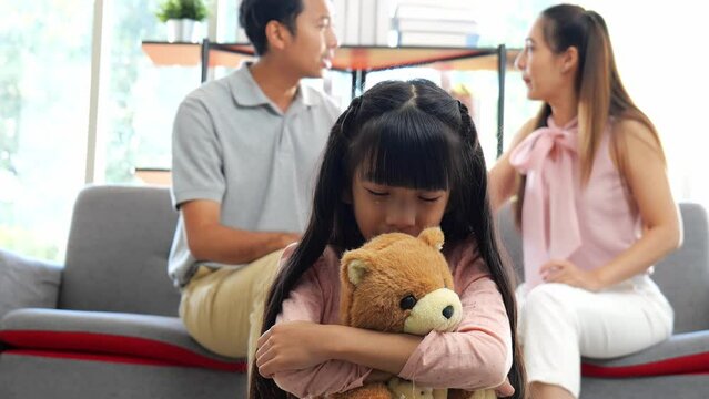 Asian childhood daughter Sitting and crying tears, hugging a doll. While the parents were arguing in the background. The concept of family violence and social problems, children's and women's rights.