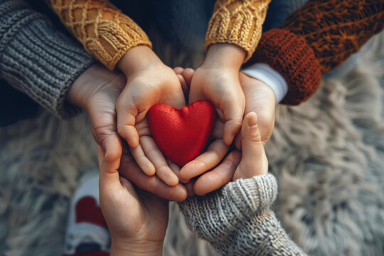 Family hands holding a single red heart top view
