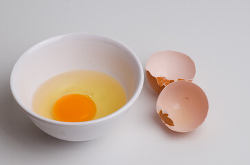 Photo of a cracked egg in a bowl with the shell beside it on a white background