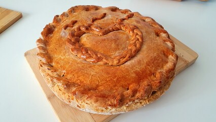 Appetizing round homemade pie with a golden crust with a heart pattern. Mom's pie, grandma's pie. Homemade baked goods made with love. Delicious homemade pie with filling on the table.