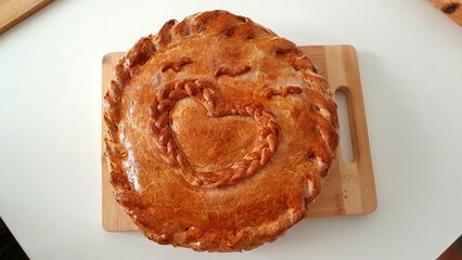 Appetizing round homemade pie with a golden crust with a heart pattern. Mom's pie, grandma's pie. Homemade baked goods made with love. Delicious homemade pie with filling on the table.