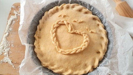 Appetizing round homemade pie with a heart pattern. Homemade baked goods made with love. Delicious homemade pie with filling on the table. Baking dough. Raw pie. Mom's pie, grandma's pie.