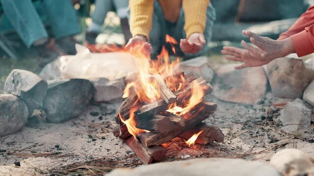 Friends, hands and camping fire in nature, group and holiday or vacation with bonfire in designated area for adventure. Bonding, together and outdoor, relax and campsite for warm or picnic in park