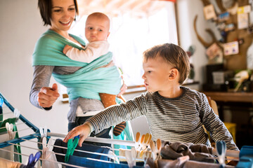 Young son helping mother with hosehold chores, hanging clothes on drying rack. Weekly chores,...
