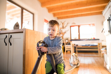 Young son helping mother with hosehold chores, vacuuming and cleaning their house. Weekly chores,...
