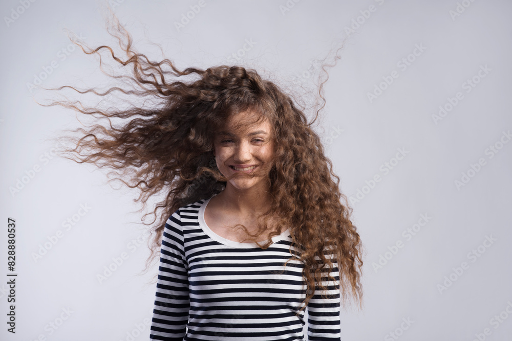 Wall mural portrait of a gorgeous teenage girl with curly hair, blowing in wind. studio shot, white background 