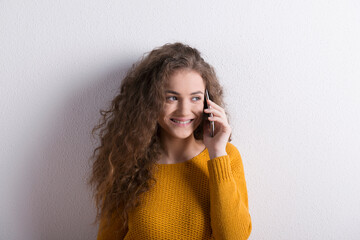 Portrait of a gorgeous teenage girl with curly hair, making phone call. Studio shot, white...