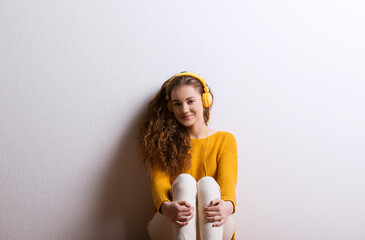 Portrait of a gorgeous teenage girl with curly hair, listening music via headphones. Studio shot,...