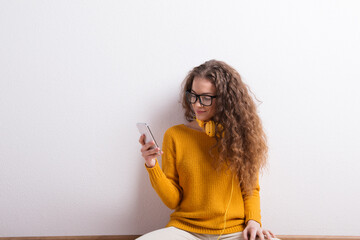 Portrait of a gorgeous teenage girl with curly hair, holding smartphone, scrolling. Studio shot,...