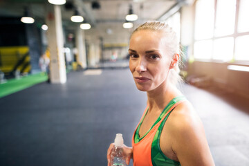 Beautiful sport woman drinking water afeter training in gym. Routine workout for woman's physical and mental health.