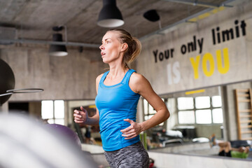 Beautiful sport woman in gym, running on treadmill. Routine workout for woman's physical and mental health.