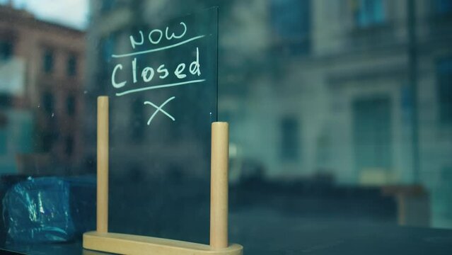 A closed business storefront in an urban area has a handwritten sign on the glass