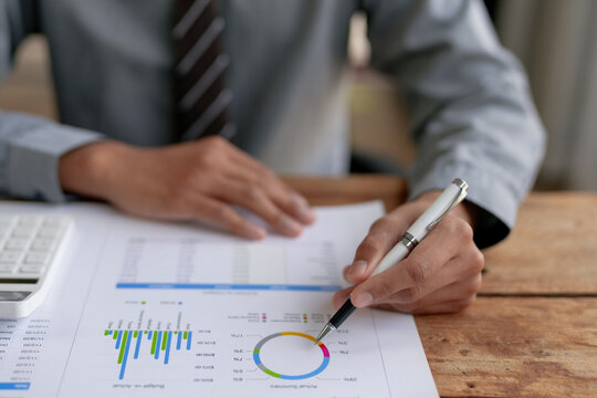Business professional analyzing financial reports and graphs with charts on a wooden desk, pointing with a pen.