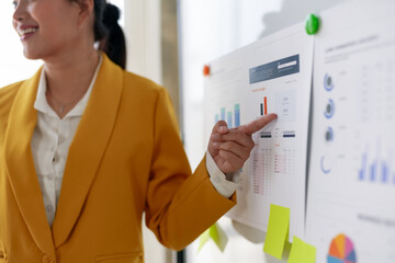 Businesswoman presenting data on a whiteboard in an office setting. Focus on growth charts,...