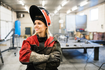 Beautiful blonde woman works as a welder in workshop, operating welding machine, wearing protective...