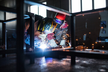 Blonde woman works as a welder in workshop, operating welding machine, wearing protective clothing...