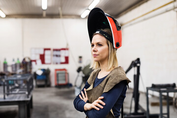 Beautiful blonde woman works as a welder in workshop, operating welding machine, wearing protective...
