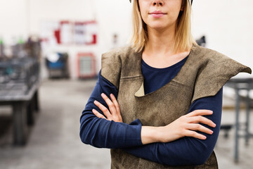 Beautiful blonde woman works as a welder in workshop, wearing leather welding apron.