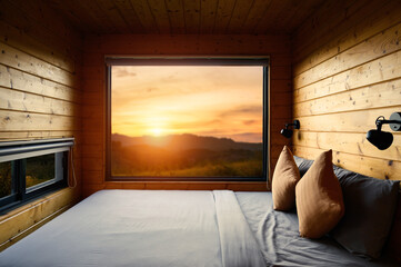 Interior of wood cabin with cozy bed during summer sunset on the window.