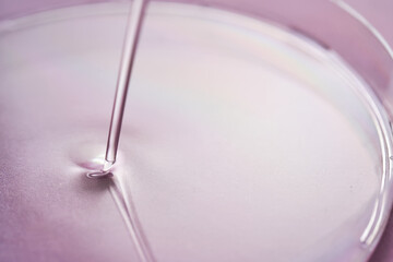 Serum or cosmetic oil flows into a transparent bowl on a purple background.