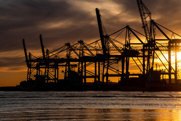 Obraz premium Silhouettes of ship to shore cranes at sunset..