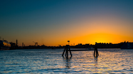 Fototapeta premium Golden sunset and city silhouette by a river.