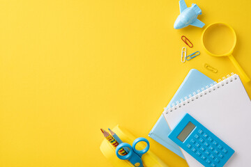 Top view of school supplies including a notebook, calculator, and pencils on a vibrant yellow background