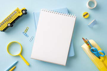 Top view of school supplies including a blank notebook, a yellow school bus, and other stationery...