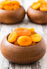 Dried apricots in wooden bowls on a rustic white wooden table, the bright orange color of the apricots contrasting with the natural brown of the bowls.