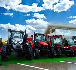 The new red agricultural tractors of various models stand in a row at the exhibition site in...