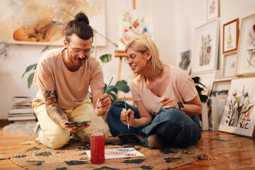 Artistic hipster couple sitting on atelier floor and painting on canvas